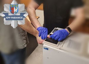 Policjant pobiera zatrzymanemu odciski palców.