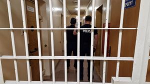 Za kratami stoi policjant i zatrzymany mężczyzna.