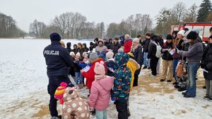 Policjanci i strażacy omawiają temat bezpieczeństwa. Zgromadzeniu na pokazie uczniowie i nauczyciele słuchają treści prelekcji.