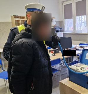 Policjant bada zatrzymanego mężczyznę alkomatem.