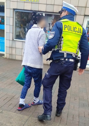 Policjant prowadzi zagubioną seniorkę.