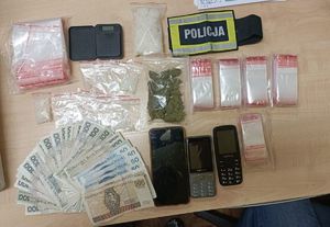 Zabezpieczone narkotyki, telefony, wagi, pieniądze. Obok nich leży opaska z napisem Policja.