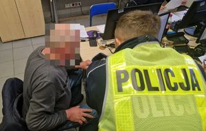 Policjant pochyla się nad zatrzymanym mężczyzną.