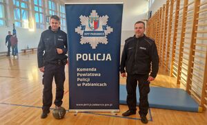 Dzielnicowi stoją pomiędzy banerem komendy. W tle widać tor przeszkód.