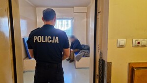 Policjant stoi w drzwiach, w tle widać mężczyznę doprowadzonego do wytrzeźwienia w policyjnej celi.