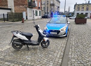 Skuter na tle policyjnego radiowozu.