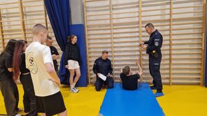 Uczeń wykonuje siady z leżenia na plecach. Czynności przyglądają się policjanci.