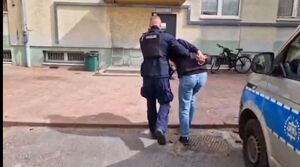 Umundurowany policjant prowadzący zatrzymanego mężczyznę.