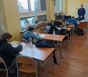 Zawodnicy rozwiązują test wiedzy pod okiem policjanta.