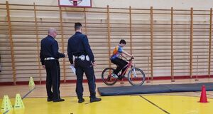 Zawodnik pokonuje rowerem tor przeszkód. Jego zmaganiom przyglądają się policjanci.