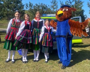 Dziewczynki ubrane w stroje ludowe stoją obok pabianickiej maskotki policyjnej.