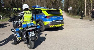 Policjanci zabezpieczający rajd rowerowy. Na zdjęciu widać również motocykl i radiowóz.