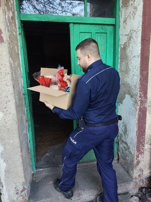 Policjant wnoszący karton z jedzeniem do budynku.