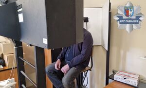 Podejrzany siedzący na urządzeniu do wykonywania zdjęć przez techników kryminalistyki znajdujący się w trakcie procedury fotografii sygnalitycznej.