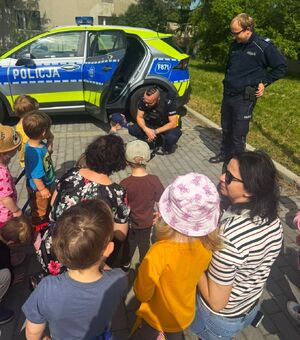Policjanci na tle radiowozu. Przed mundurowymi stoją dzieci.
