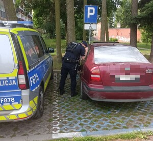 Policjant zaglądający przez szybę do samochodu.