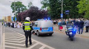 Policjant oraz policyjna flota na tle przechodzącej procesji.
