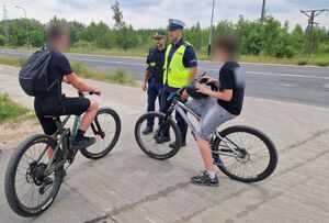 Policjant i strażnik miejski kontrolują dwóch rowerzystów.