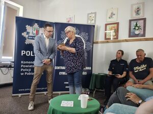 Seniorka pokazuje nieumundurowanemu policjantowi telefon.
