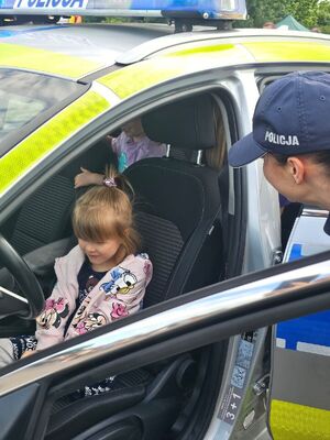 Dziecko siedzi w radiowozie, obok znajduje się policjantka.