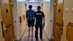 Umundurowany policjant stoi z zatrzymanym mężczyzną.