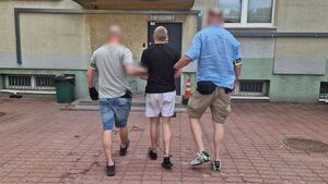 Dwóch nieumundurowanych policjantów prowadzi zatrzymanego mężczyznę.