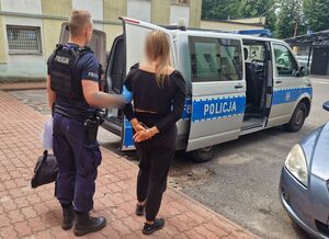 Umundurowany policjant stoi z zatrzymaną kobietą przy radiowozie.
