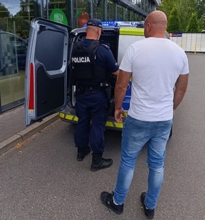 Przy radiowozie stoi dwóch policjantów. Jeden jest umundurowany