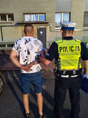 Umundurowany policjant stoi z zatrzymanym mężczyzną.