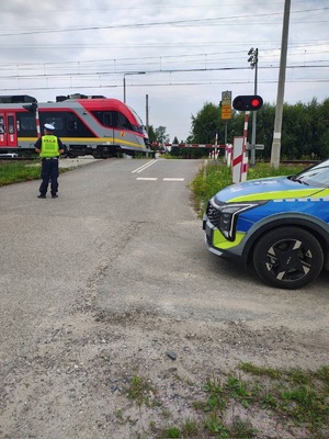 funkcjonariusz stoi przed zamkniętym przejazdem, w tle nadjeżdża pociąg