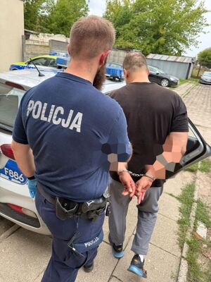 umundurowany policjant prowadzi zatrzymanego do radiowozu oznakowanego