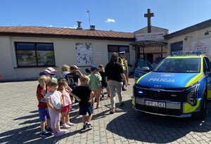 Dzieci i radiowóz przed budynkiem przedszkola.