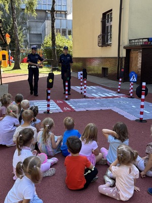 policjantki rozmawiają z grupą przedszkolną, w tle jest też mata edukacyjna autochodzik