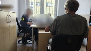 nieumundurowany policjant z opaską na ręce z napisem policja prowadzi czynności z zatrzymanym