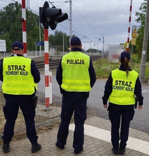 umundurowany policjant w kamizelce odblaskowej wraz z funkcjonariuszami Straży Ochrony Kolei patrolują rejon przejazdu kolejowego