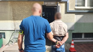nieumundurowany policjant z opaską na ręce trzyma zatrzymanego