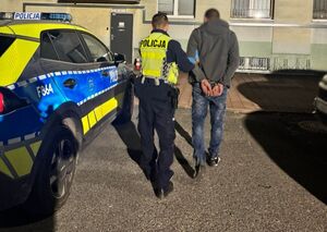 umundurowany funkcjonariusz prowadzi zatrzymanego