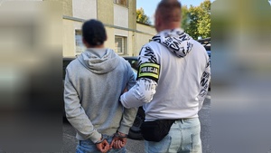 nieumundurowany funkcjonariusz z opaską Policja prowadzi zatrzymanego